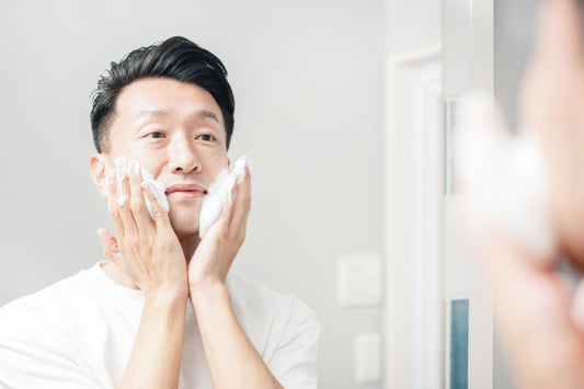 Man in bathroom applying Korean skincare cleanser foam to his face in front of the mirror, embodying the K-Wonders K-Beauty routine for men.
